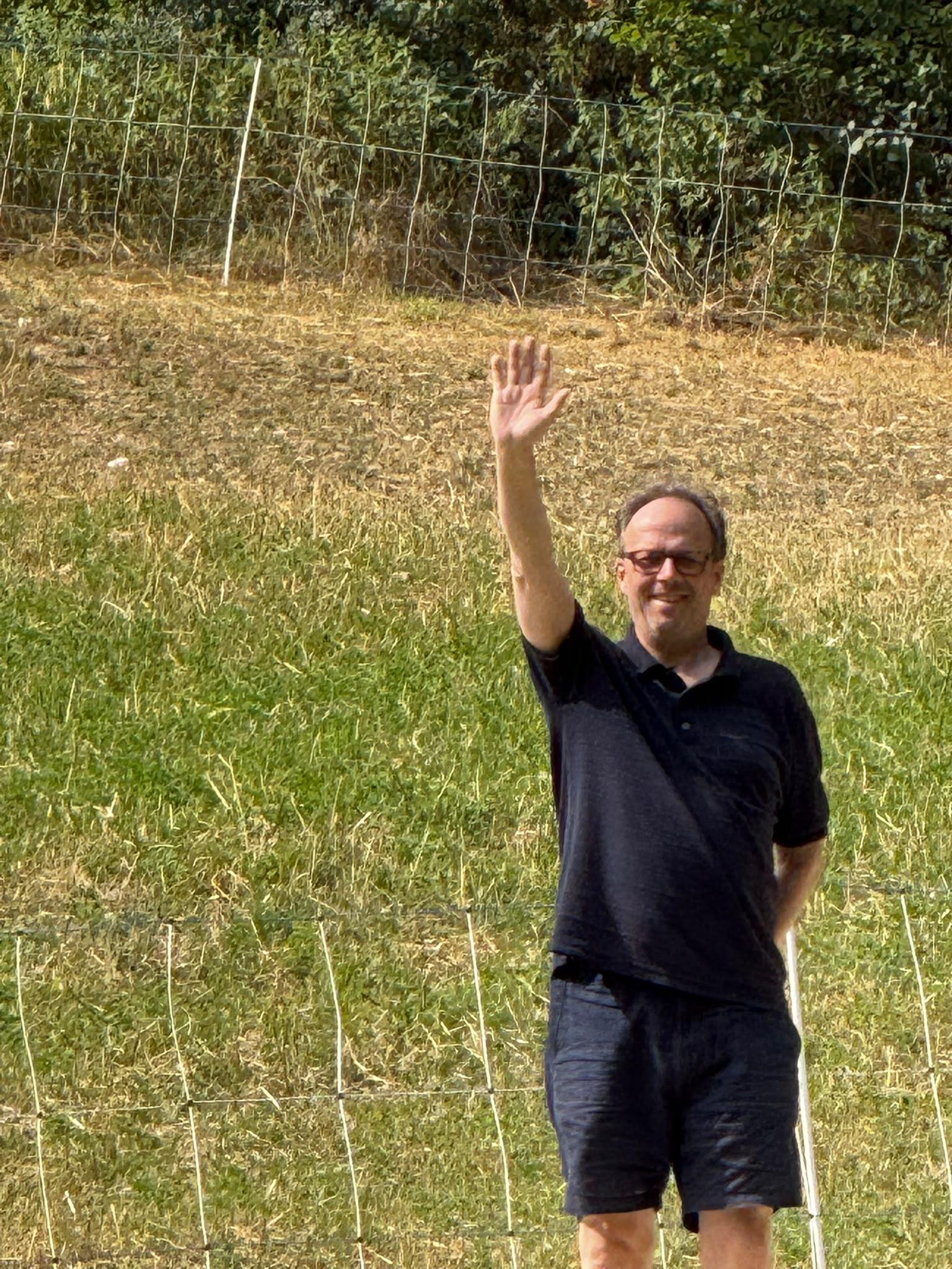 Ein Mann winkt vor einer gemähten Wiese am Waldrand
